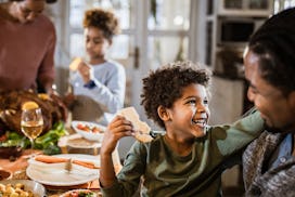 Happy Black boy talking to his father during Thanksgiving day at dining table. There are people in t...