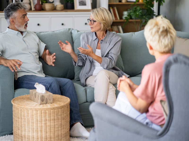 A mature gray-haired married couple are looking at each other during a therapy session with a counci...