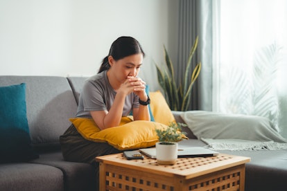 Asian woman feeling lonely thinking about problem sitting on sofa in living room at home.