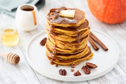 Pumpkin spice pancakes stack on white plate served with butter in roundup of canned pumpkin recipes