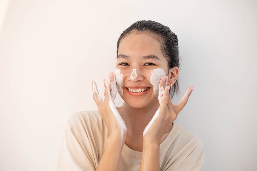 Face Skin Care. Funny Asian Woman Cleaning Facial Skin with Foam Soap. Happy Girl Cleansing Face App...