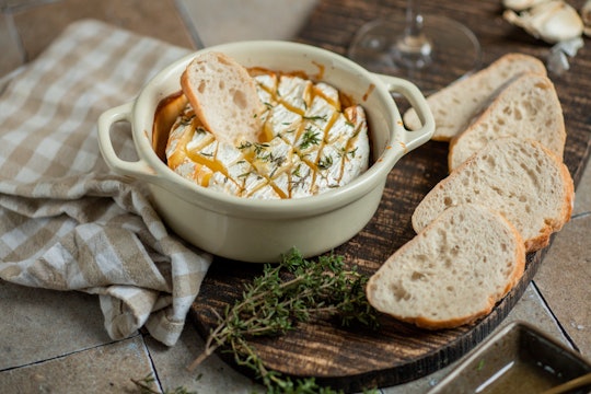 Baked Brie cheese with Thyme Herbs, Honey and white wine in rustic kitchen with baguette bread