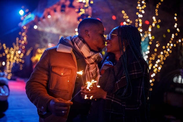 Portrait of romantic young couple having fun at the concert outside, waving sparklers, and kissing o...