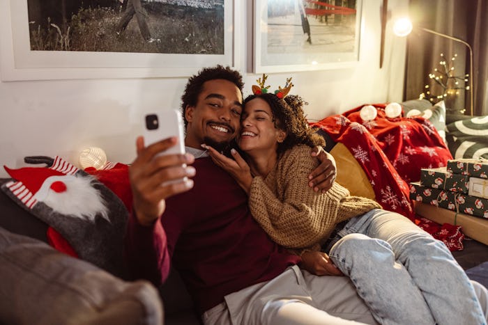 Happy young African-American couple spending time at home during winter holidays. Young man taking s...