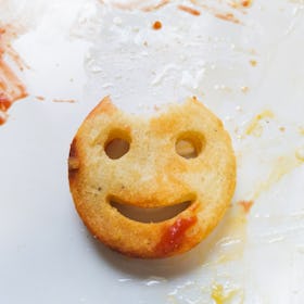 Potato smile with piece missing from its head on a plate with smeared ketchup.