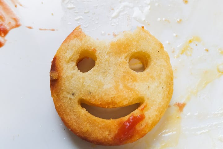 Potato smile with piece missing from its head on a plate with smeared ketchup.
