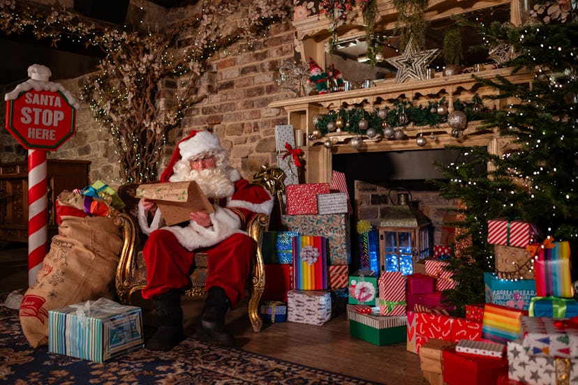 Man dressed as Santa reading a list titled 'naughty or nice' surrounded by presents. There is a Chri...