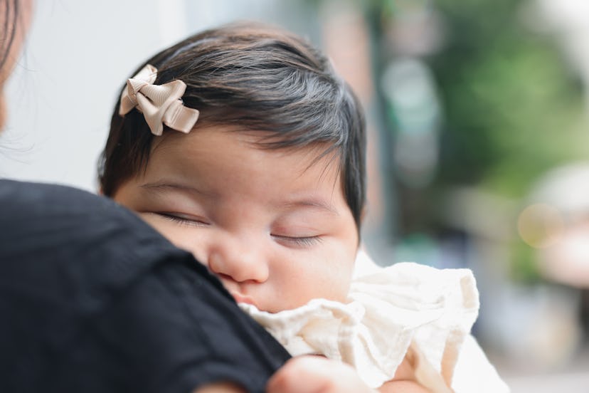 Close up portrait of asian baby girl sleeping in her parents arms in article about infants getting R...
