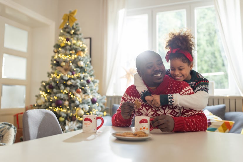 Father and daughter drinking tea and eating cookies. They are wearing Christmas sweaters and having ...