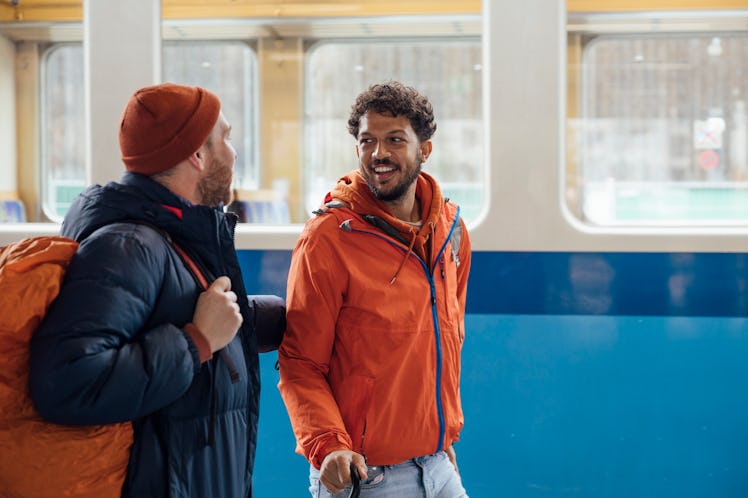 Waist-up shot of a same-sex couple walking a train platform together. They are both wearing warm clo...