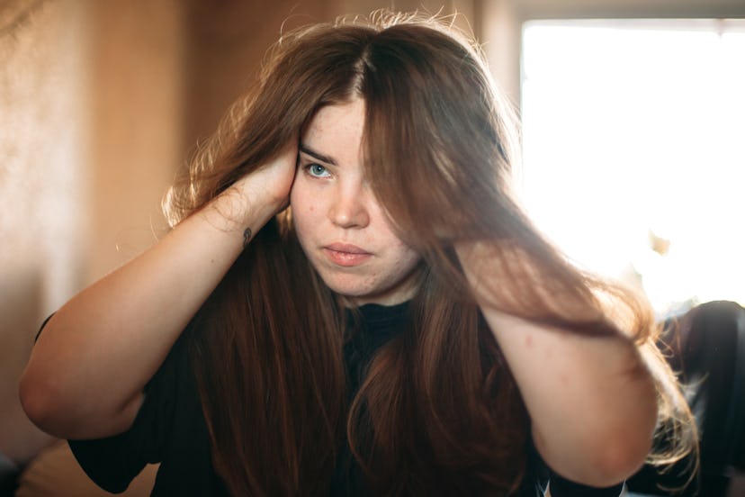 Beautiful young woman holding her head while looking in the mirror at home