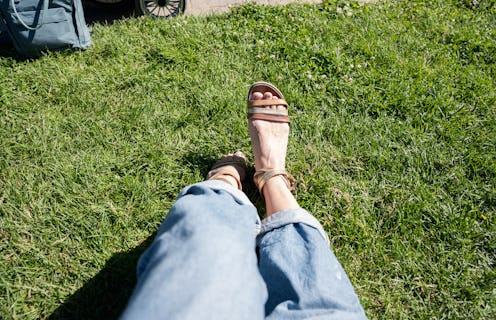 Close up of female legs Wearing sandals and Jeans on Green grass at warm sunny day