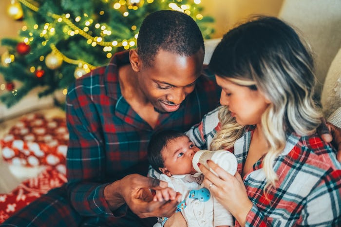 Young mother feeding the baby with feeding bottle against the Christmas tree