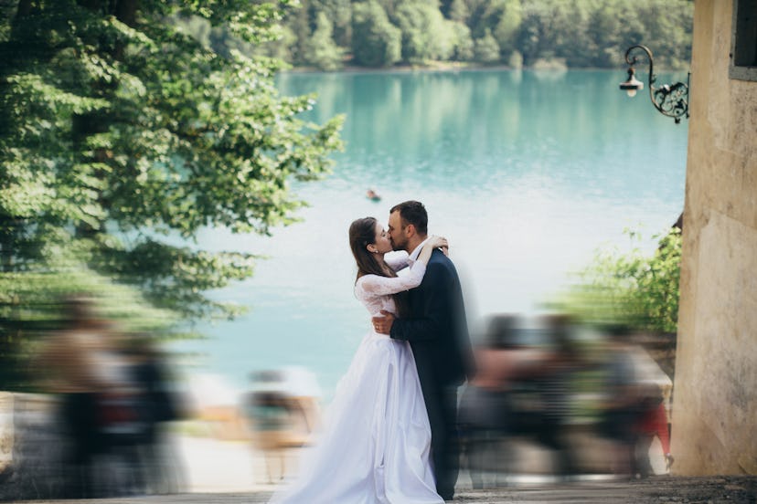 Newlyweds kiss on the wide staircase that goes to the beautiful blue lake. Bride has long dark hair....