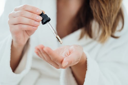Woman drips cosmetic oil onto her palm to massage her scalp and improve the quality and beauty of he...