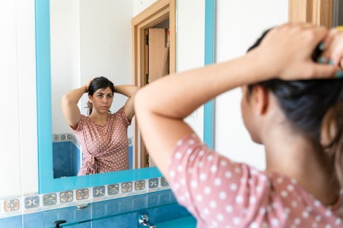 Back view of unrecognizable female in casual clothes standing in front of mirror and taking photo of...