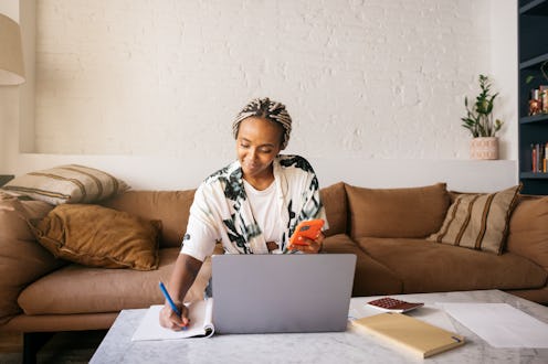 Woman sitting on a sofa and using a laptop at a table in her living room while working remotely from...
