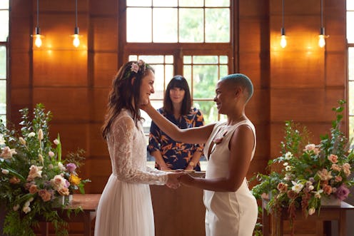 Two girls stand at the altar about to be married holding hands staring at each other