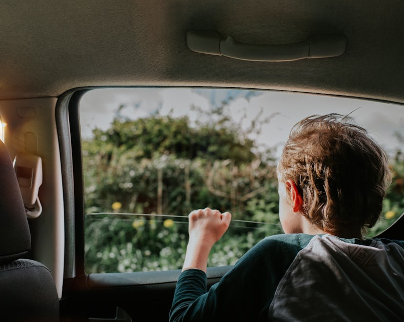 Young child looks eagerly out of a moving cars window. Trees and countryside are visible out of the ...