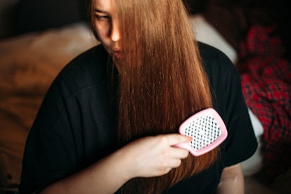 Young woman brushing her hair sitting on bed at home