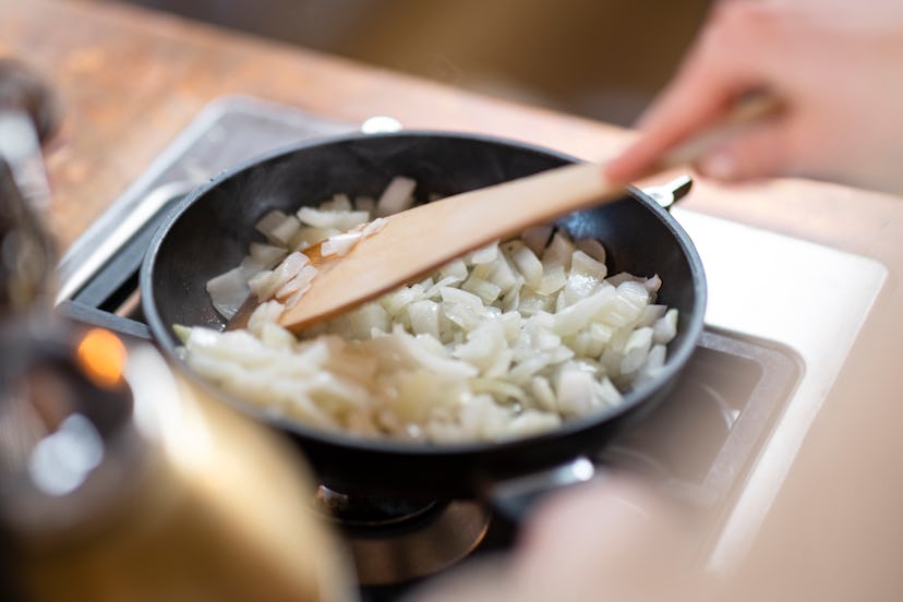 Close up of onions being fried in a frying fan. An unrecognisable person is stirring them.