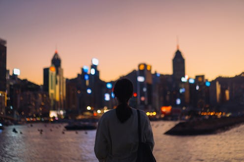 Rear view of young Asian female tourist overlooking the beautiful iconic city skyline of Hong Kong a...