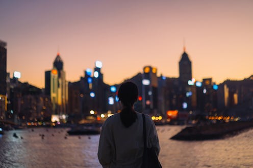 Rear view of young Asian female tourist overlooking the beautiful iconic city skyline of Hong Kong a...