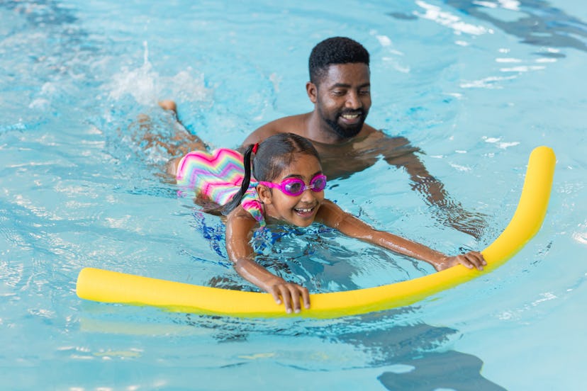 A man teaching his young daughter how to swim in a swimming pool in as an experience gift idea.