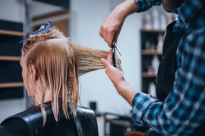 Rear view of blond woman cutting hair at hairdresser