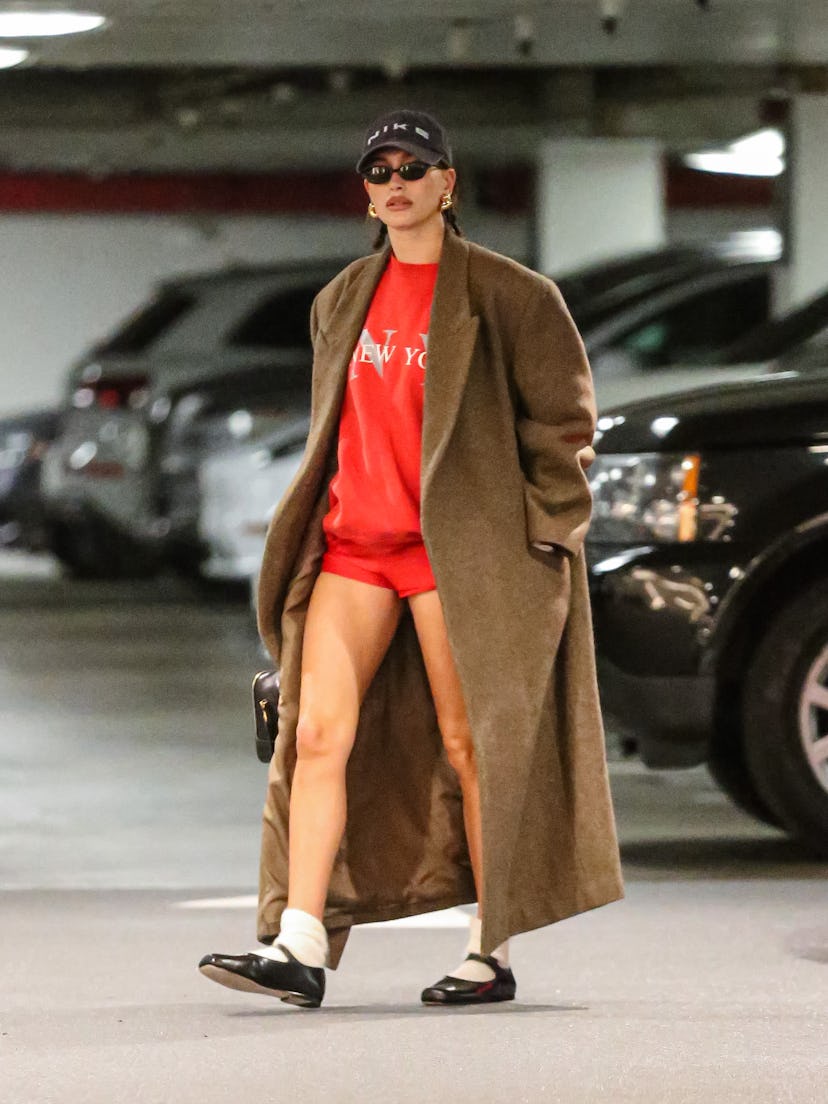 Hailey Bieber wears a coat, red sweatshirt, short, and more on December 14, 2023.