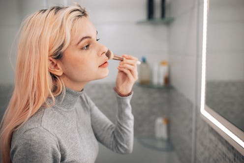 Concentrated young Caucasian woman standing in bathroom in the morning doing her make up routine
