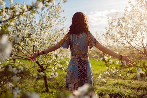 Rear view of young woman enjoying carefree spring day in blossoming orchard.
