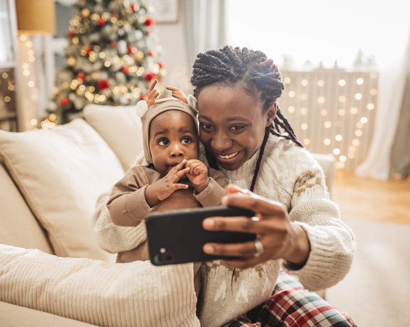 Mother and her baby playing and having fun by the Christmas tree on Christmas morning.