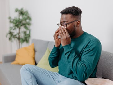 Young man experiencing sickness while sitting on living room couch