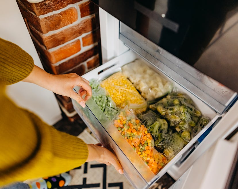 Woman putting container with frozen mixed vegetables to refrigerator