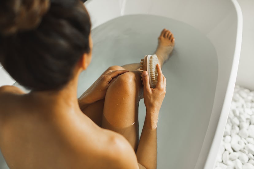 Unrecognizable Woman Massaging her Knee with Massage Brush while Taking a Relaxing Bath. Young Woman...