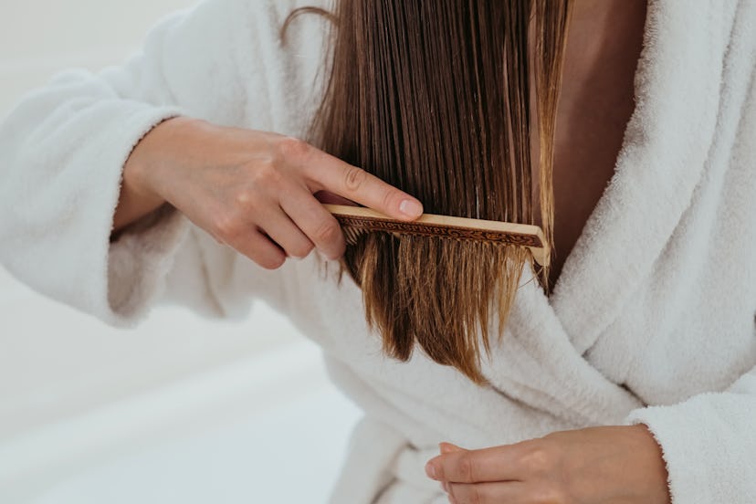 Unrecognised woman carefully combing her hair with a wooden comb. Closeup, Treatment for split ends ...
