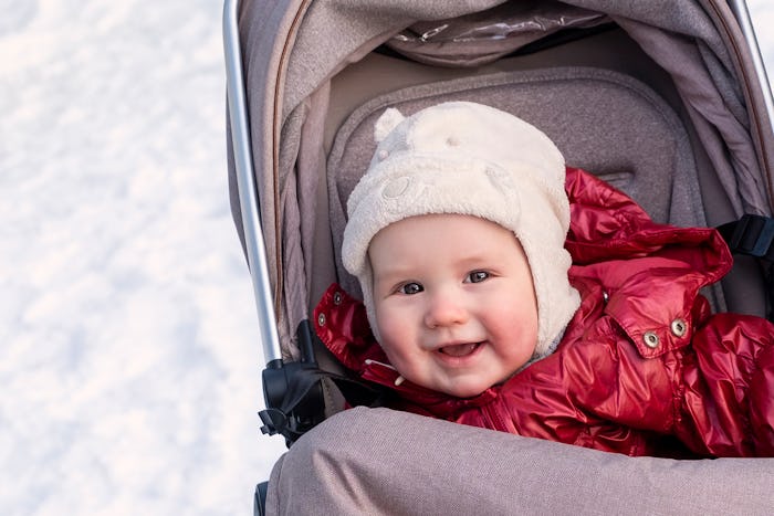 A one-year-old baby, a Caucasian boy, lies in a baby carriage and smiles. Walk in the winter in the ...