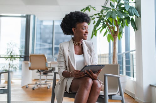 Content black female manager sitting in a chair in a beautiful office and looking through the window...