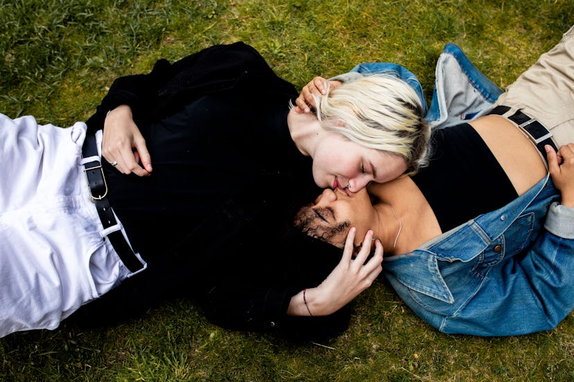 A lesbian couple lying in the grass, kissing