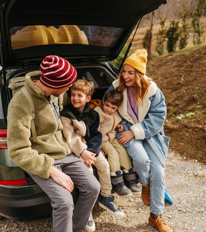 Photo of a smiling, cheerful family sitting in the trunk of their car, all packed up and ready for a...