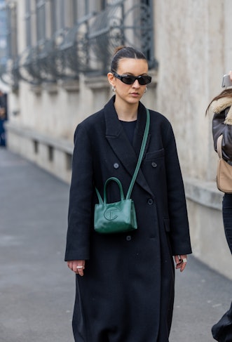 MILAN, ITALY - FEBRUARY 23: A guest wears green bag, black coat outside Prada during the Milan Fashi...