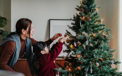 Young Asian mother and lovely little daughter decorating Christmas tree at home together; tips to ma...
