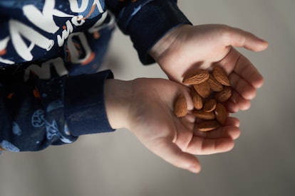 Toddler hands holding whole almonds in a story about whether it's safe for toddlers to eat whole mix...