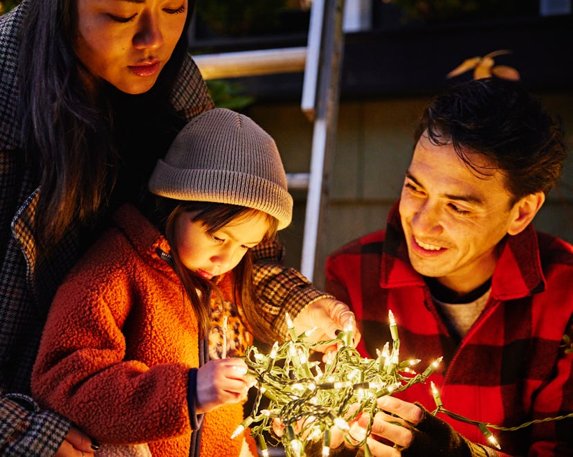 Medium shot of daughter holding lights while decorating home for Christmas with family on winter eve...