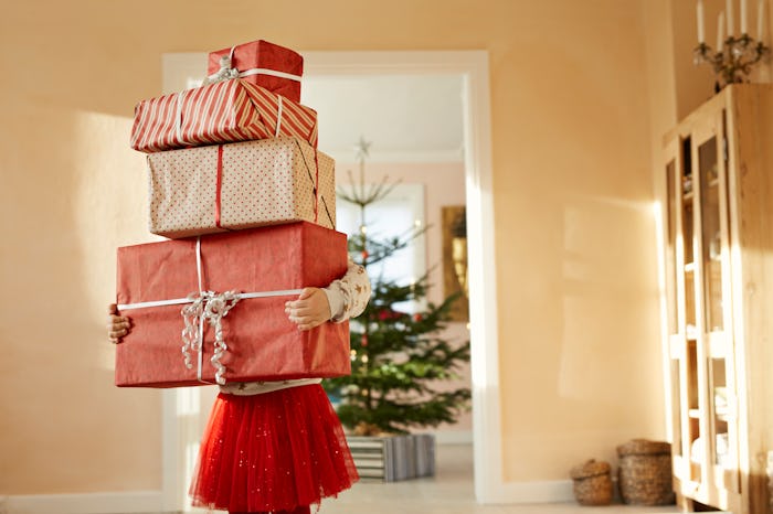 Little girl holding tall stack of christmas presents, excessive gift giving is a thing in her family...
