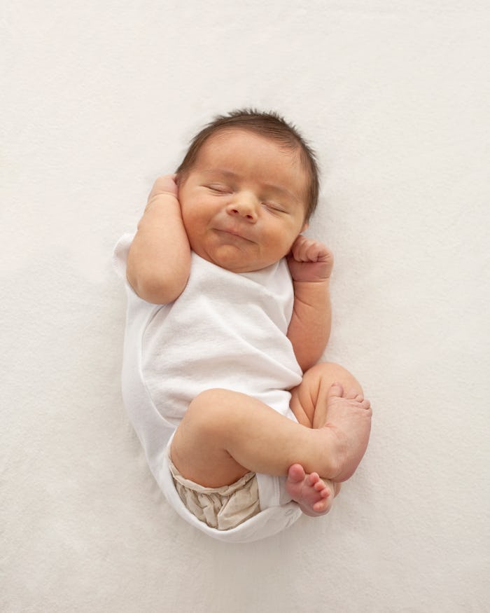 Newborn baby scrunched up on a white blanket, in a story answering the question, why do babies do th...