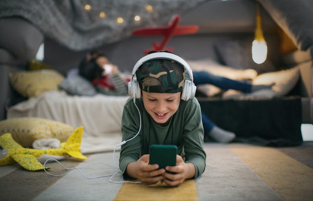 Boy playing game on his smart phone at his room. He is wearing headphones, smiling and enjoying the ...