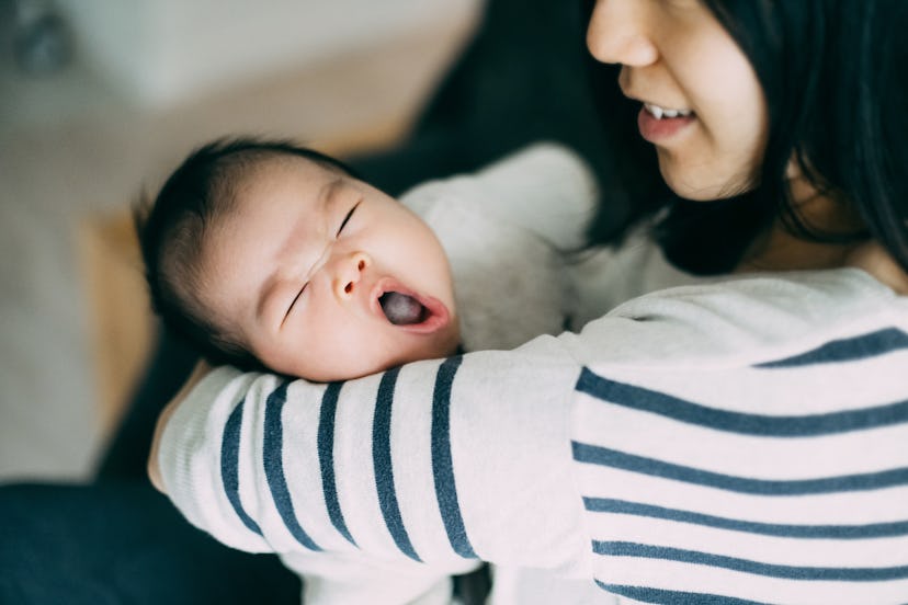 Caring Asian young mother holding yawning baby in an article about sleep regression, what they are w...