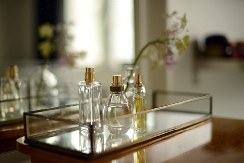 perfume bottles and a vase with flower on a glass tray by a mirror
